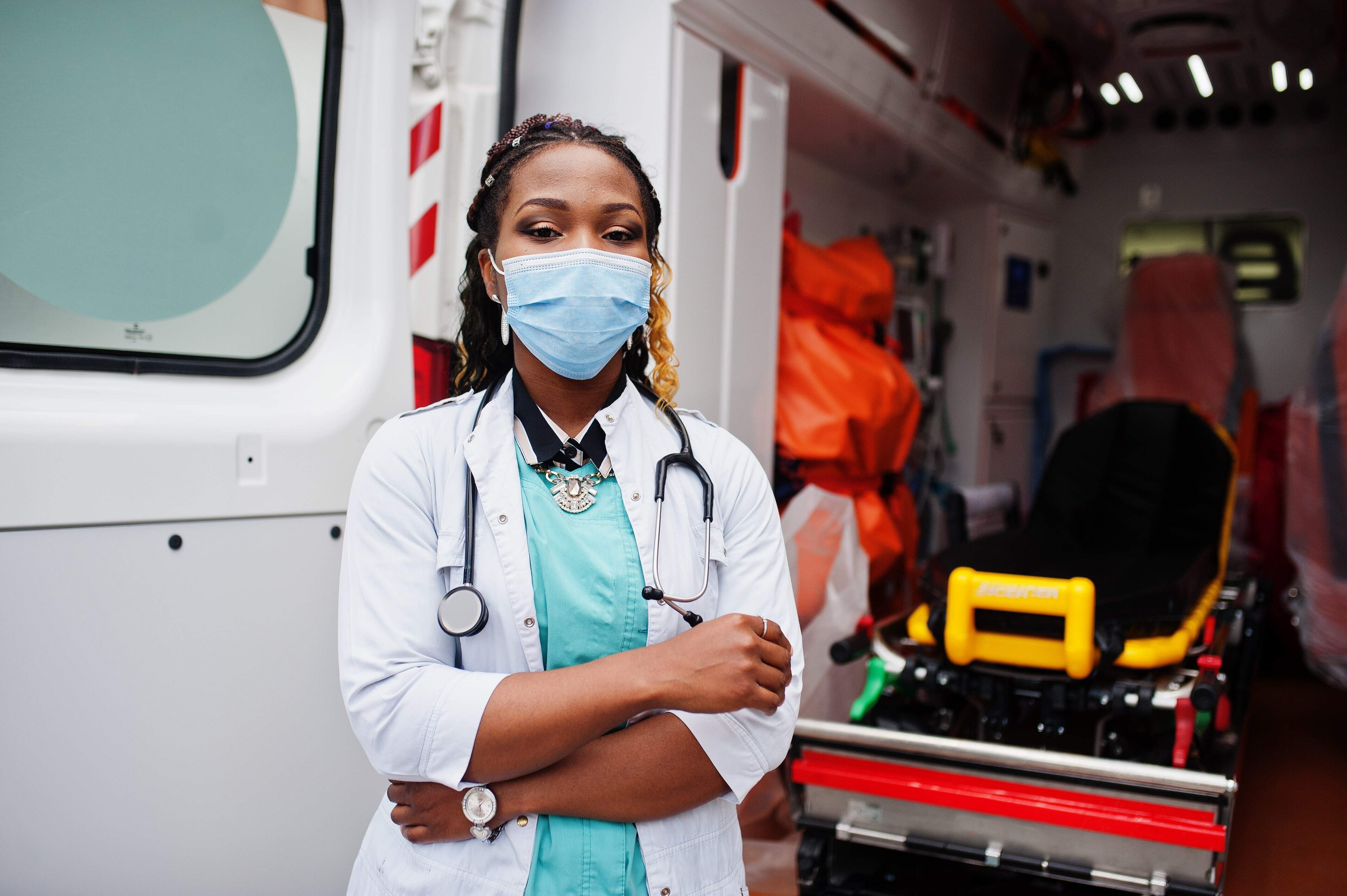 african-american-female-paramedic-face-protective-medical-mask-standing-front-ambulance-car-min